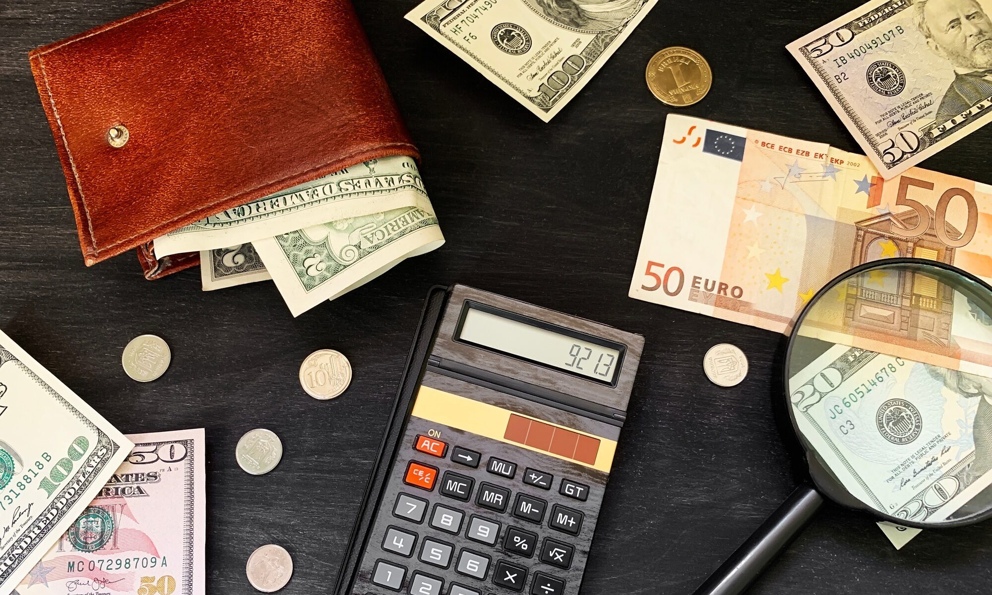 Calculator, cash money and wallet on black wooden background