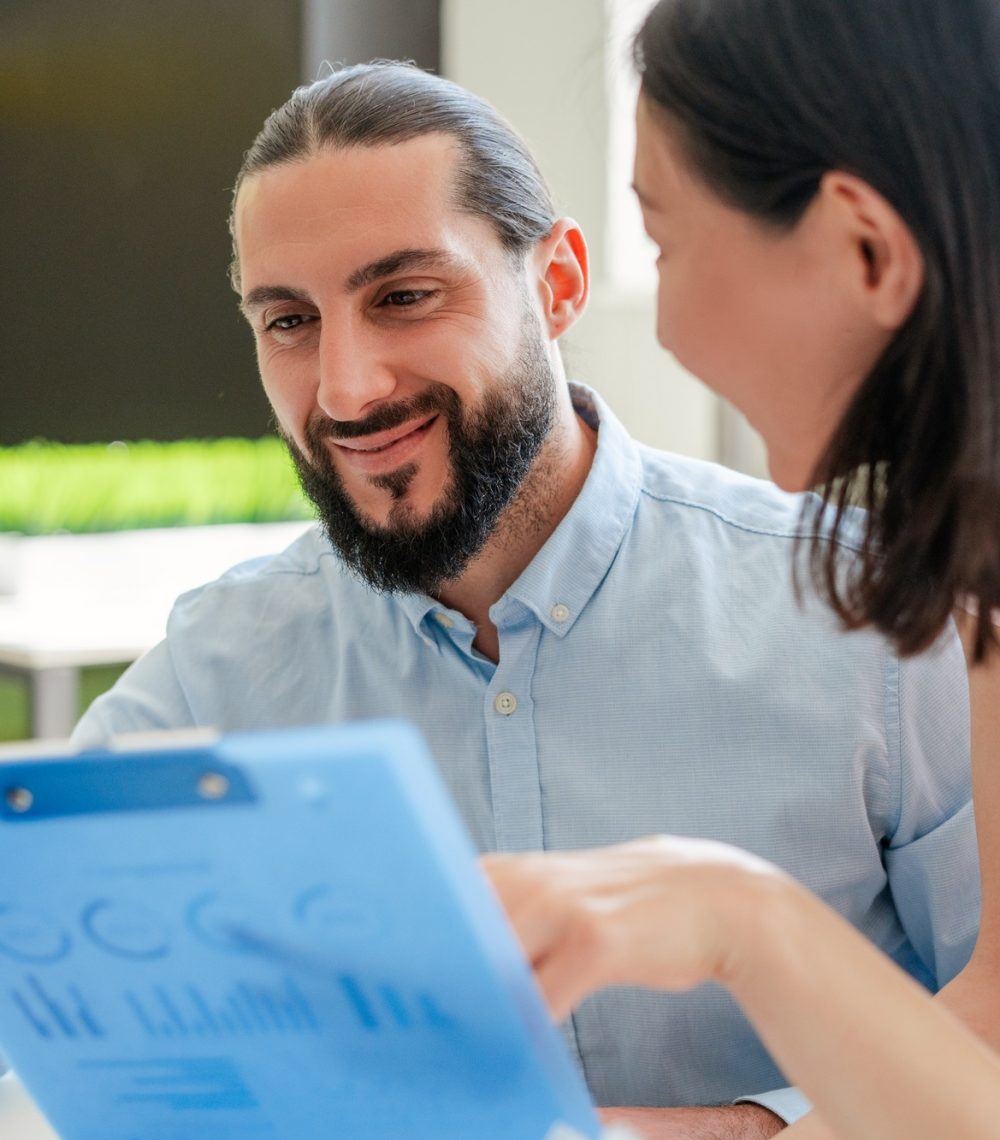 Handsome confident Arab ceo businessman holding documents, his beautiful Asian secretary talking